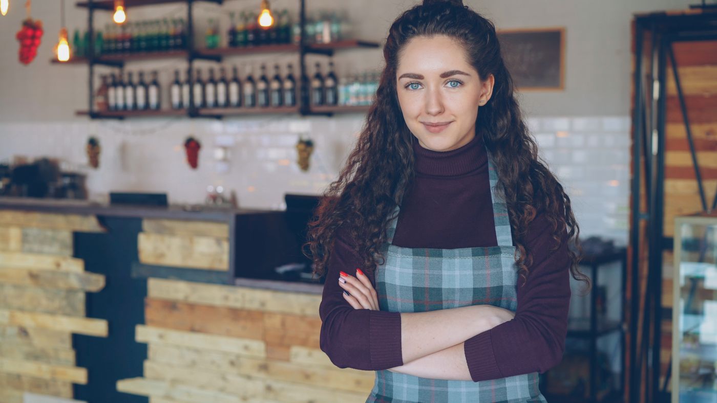 Dueña de una cafetería sonriendo mientras cuelga el cartel de «Abierto».